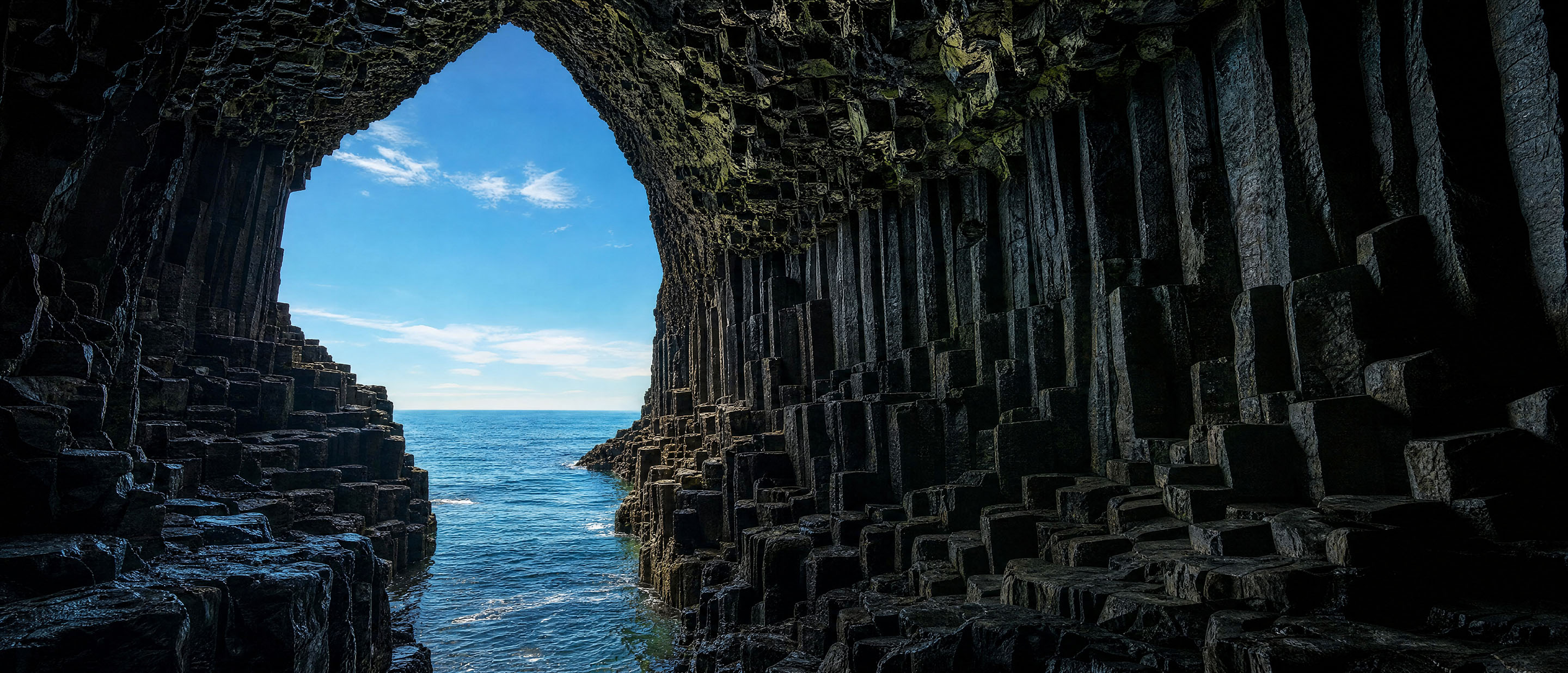 Cueva de columnas de basalto frente al mar, con la salida hacia el océano al fondo